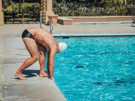 An adult male athlete poised to dive into a turquoise swimming pool.