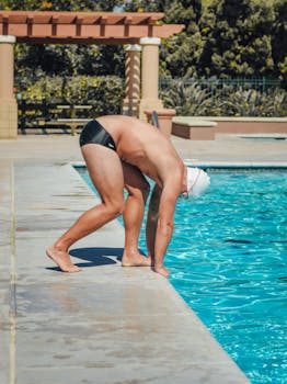 Male swimmer in swimwear ready to dive into a clear blue outdoor pool on a sunny day.