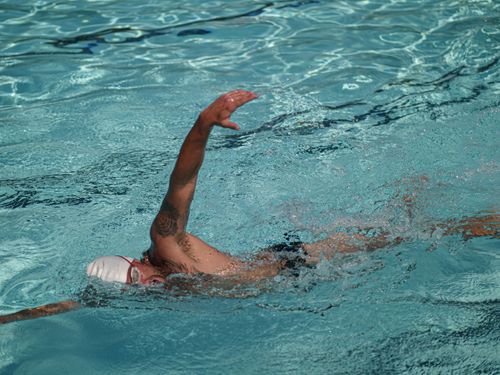 Free A tattooed man wearing goggles swimming freestyle in a clear blue pool. Stock Photo