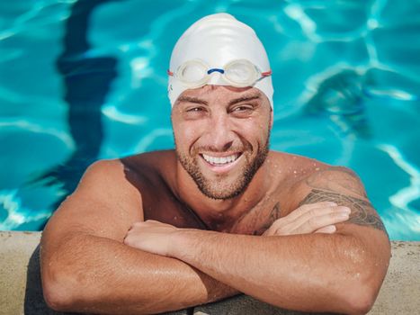 Portrait of a smiling male swimmer in the pool wearing a swim cap and goggles.