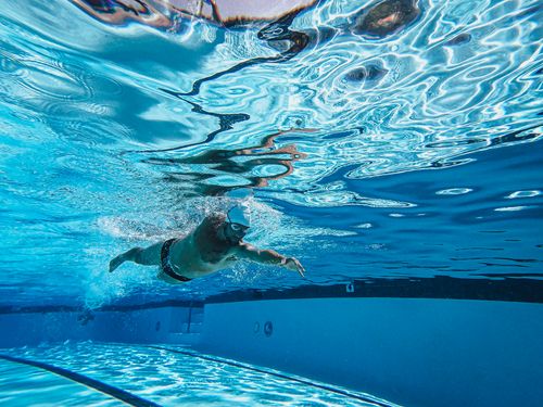 Free Dynamic underwater photo of a man swimming freestyle in a pool wearing goggles and a cap. Stock Photo