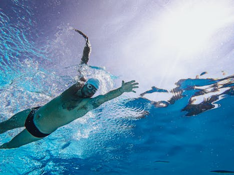 A male swimmer performing a freestyle stroke underwater with sunlight streaming above, showcasing intense athleticism.