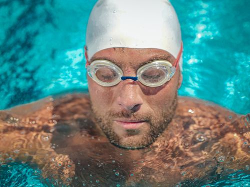 Free Close-up of a male swimmer wearing goggles in a pool, showcasing concentration and skill. Stock Photo