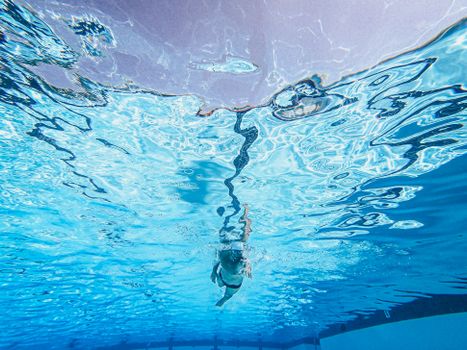 An underwater shot of a child swimming in a pool, showcasing freestyle swimming skills.