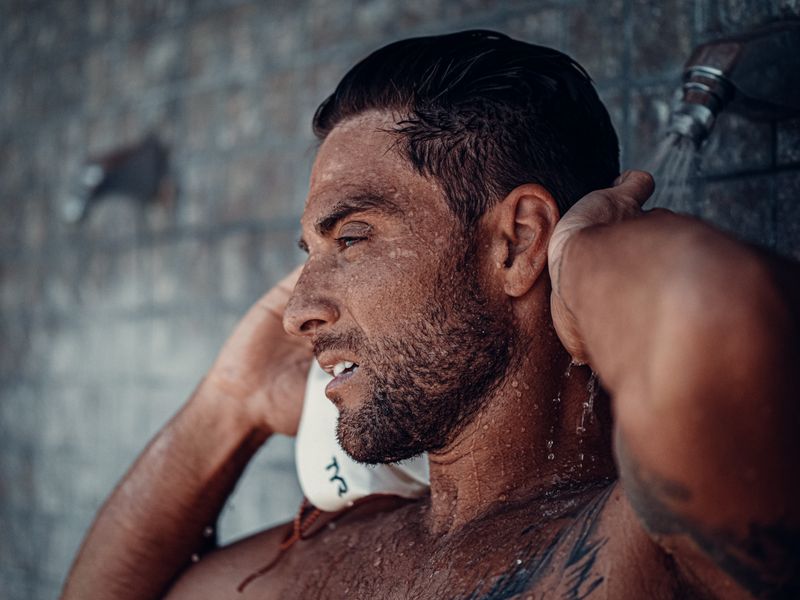 Close-up of a shirtless man enjoying an outdoor shower, emphasizing relaxation and refreshment.