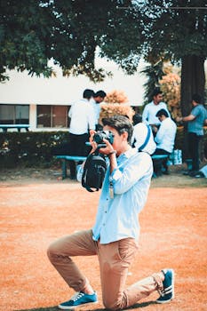在热闹的公园聚会上，一名年轻人跪下拍照，展示他的摄影技巧