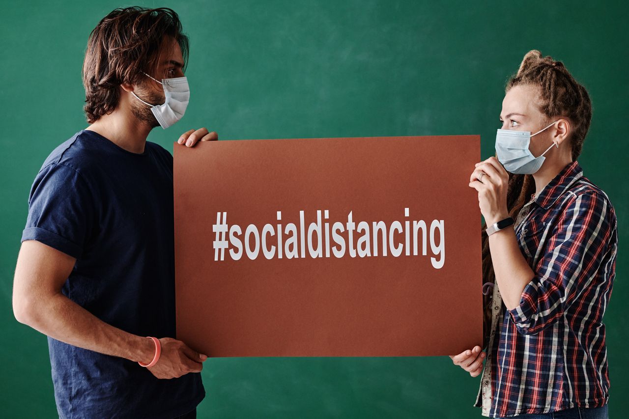 man and woman wearing masks holding a social distancing sign highlight