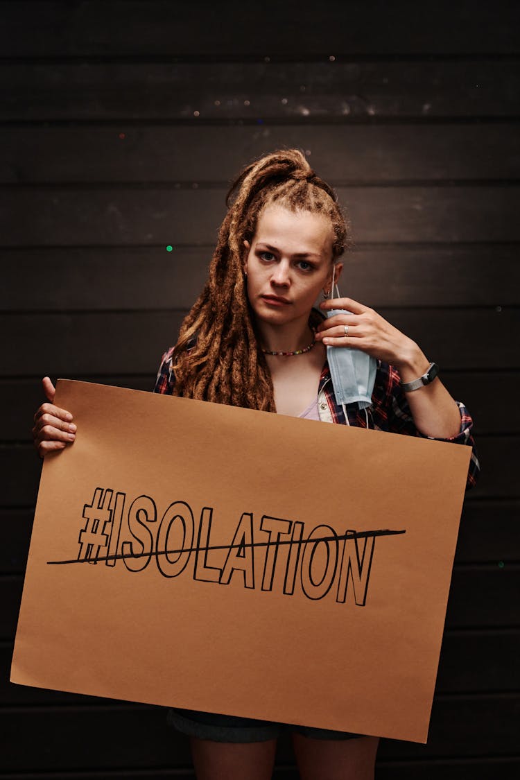 A Woman Removing Her Face Mask While Holding A Sign