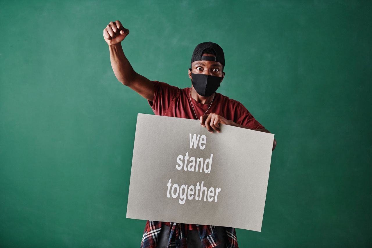 man holding a sign saying we stand together wearing a face mask emphas