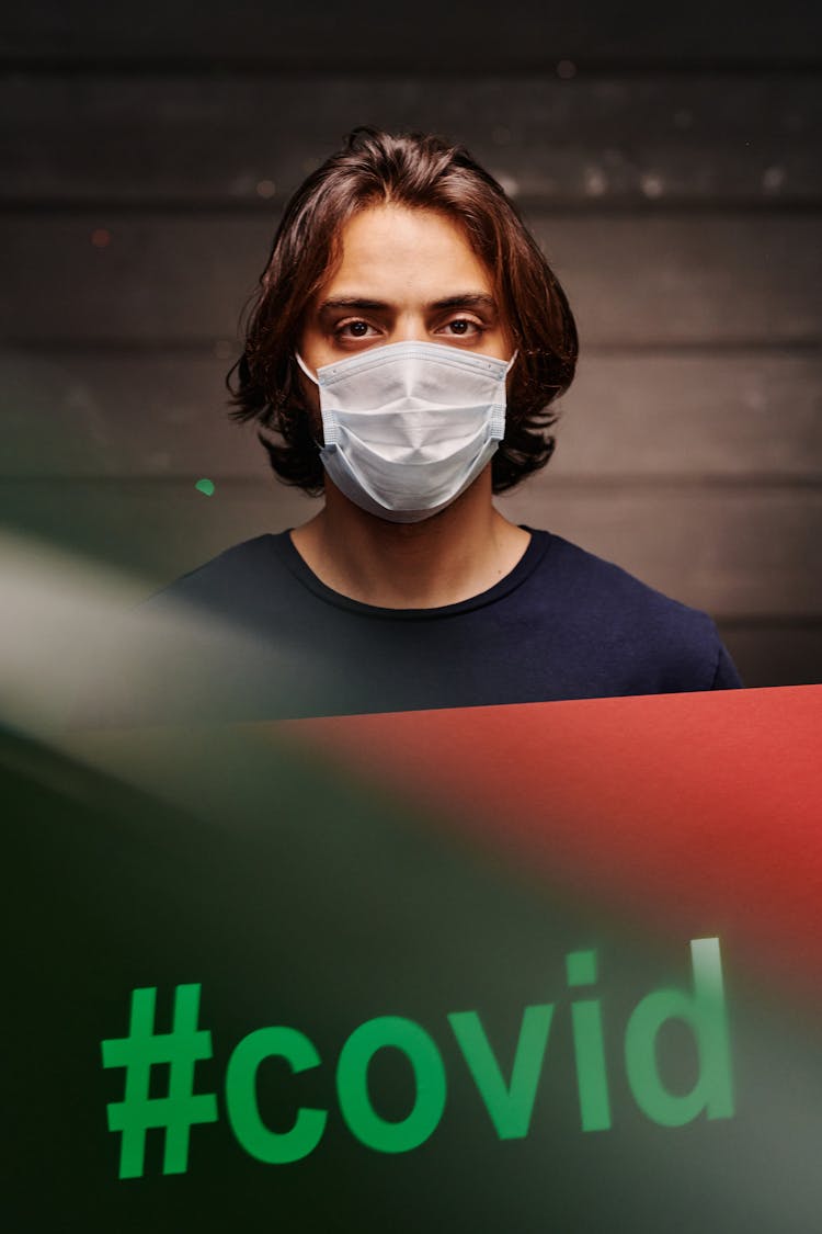 A Long-Haired Man With Face Mask Holding A Poster