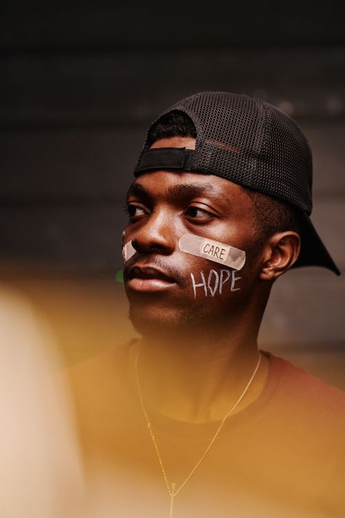 Free Close-up of a man wearing a cap with Band-Aids bearing the words 'Care' and 'Hope' on his face. Stock Photo