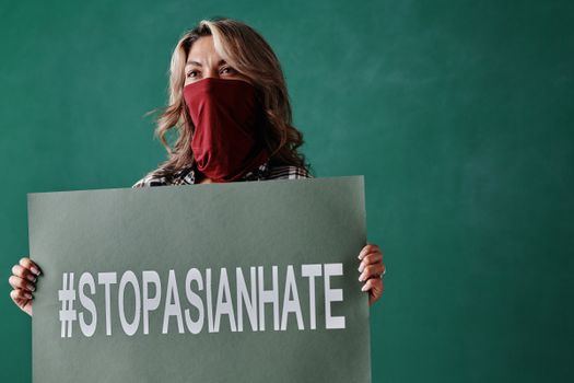 A woman in a bandana holds a #stopasianhate placard against a green backdrop.