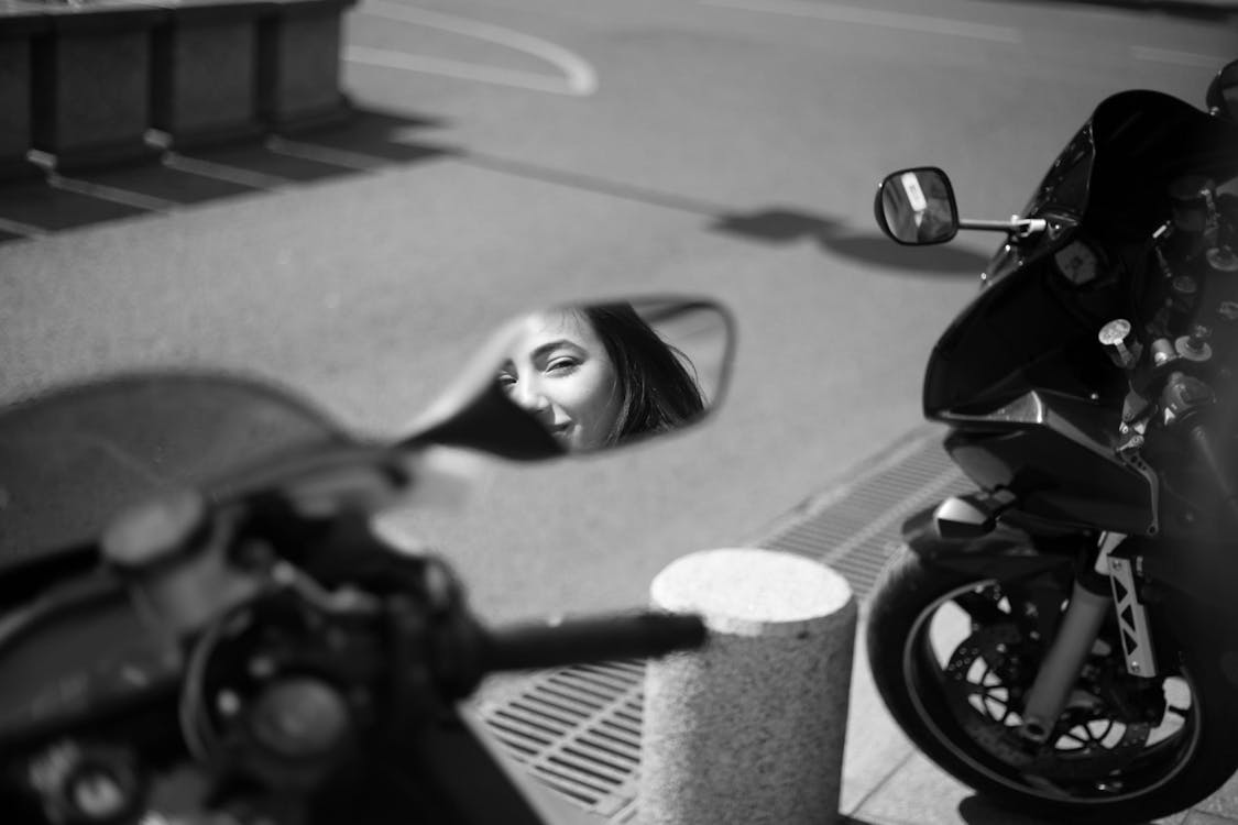 Grayscale Photo of a Woman's Reflection in a Side Mirror on a Motorcycle