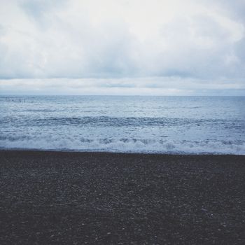 Serene pebble beach with gentle waves and a moody, overcast sky, perfect for relaxation.