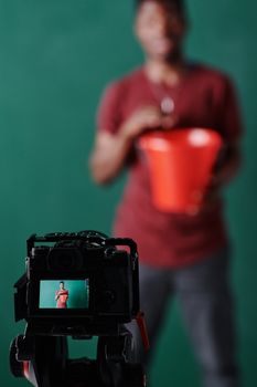 Man in red shirt with a red bucket blurred, camera screen focused on him.