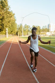 A young man exercises with a jump rope on an outdoor track, under a clear sky.