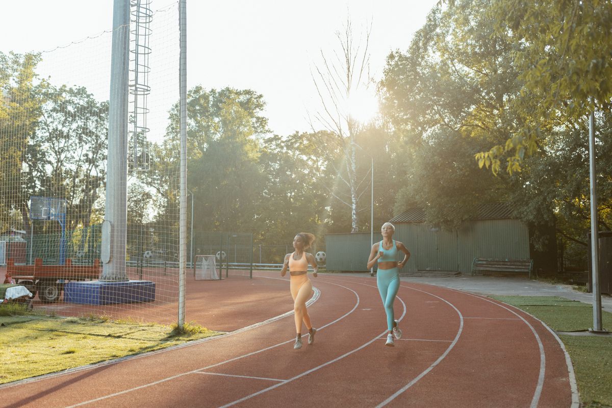 Two women jogging side by side on an outdoor track in the morning sun