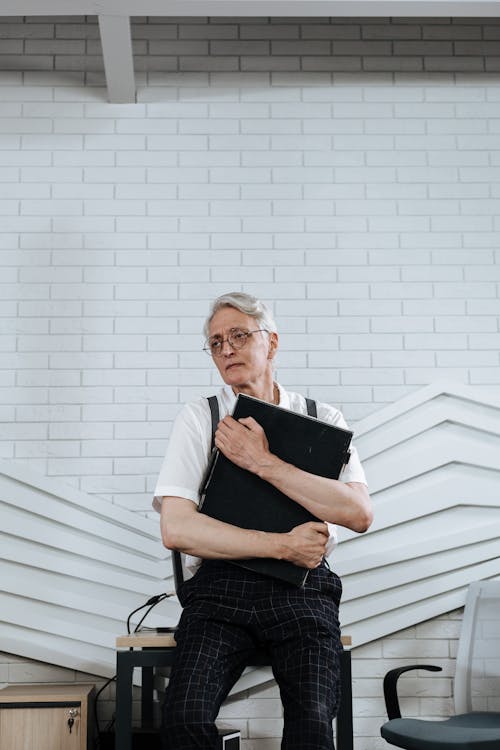 Man Sitting on Table Holding a Black Clutch Bag