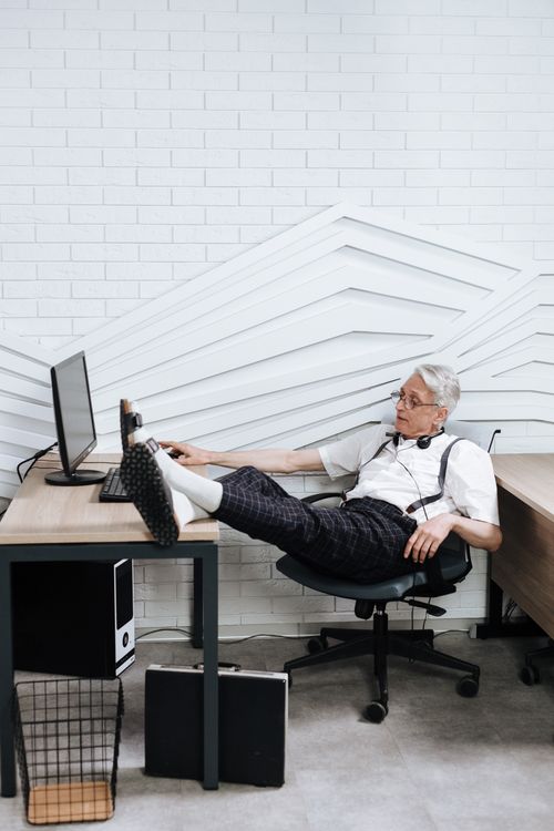 Free Senior man taking a break at desk with feet up, showcasing a casual office environment. Stock Photo