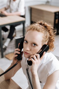 Focused young woman multitasking with phones in a professional office setting.