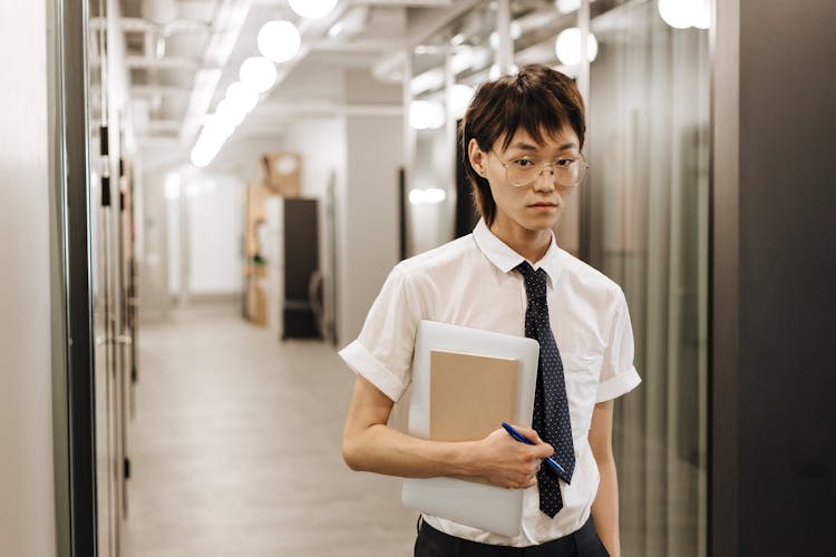 A Man Walking On The Office Hallway While Carrying A Tablet And A Notebook