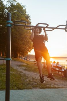Young man performing pull-up exercise outdoors during sunset near a scenic lake.