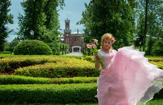 A woman in a pink dress standing in a garden holding flowers, surrounded by lush greenery and a castle in the background.