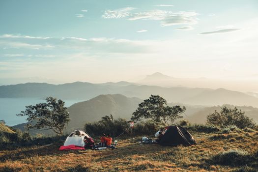 A serene camping setup with tents on a mountain side and a breathtaking horizon view.