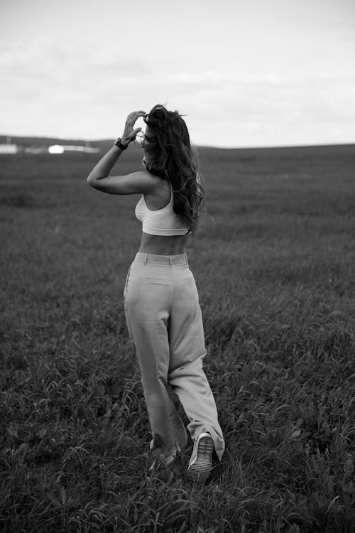 Grayscale Photo of a Woman in White Tank Top Walking on the Grass Field