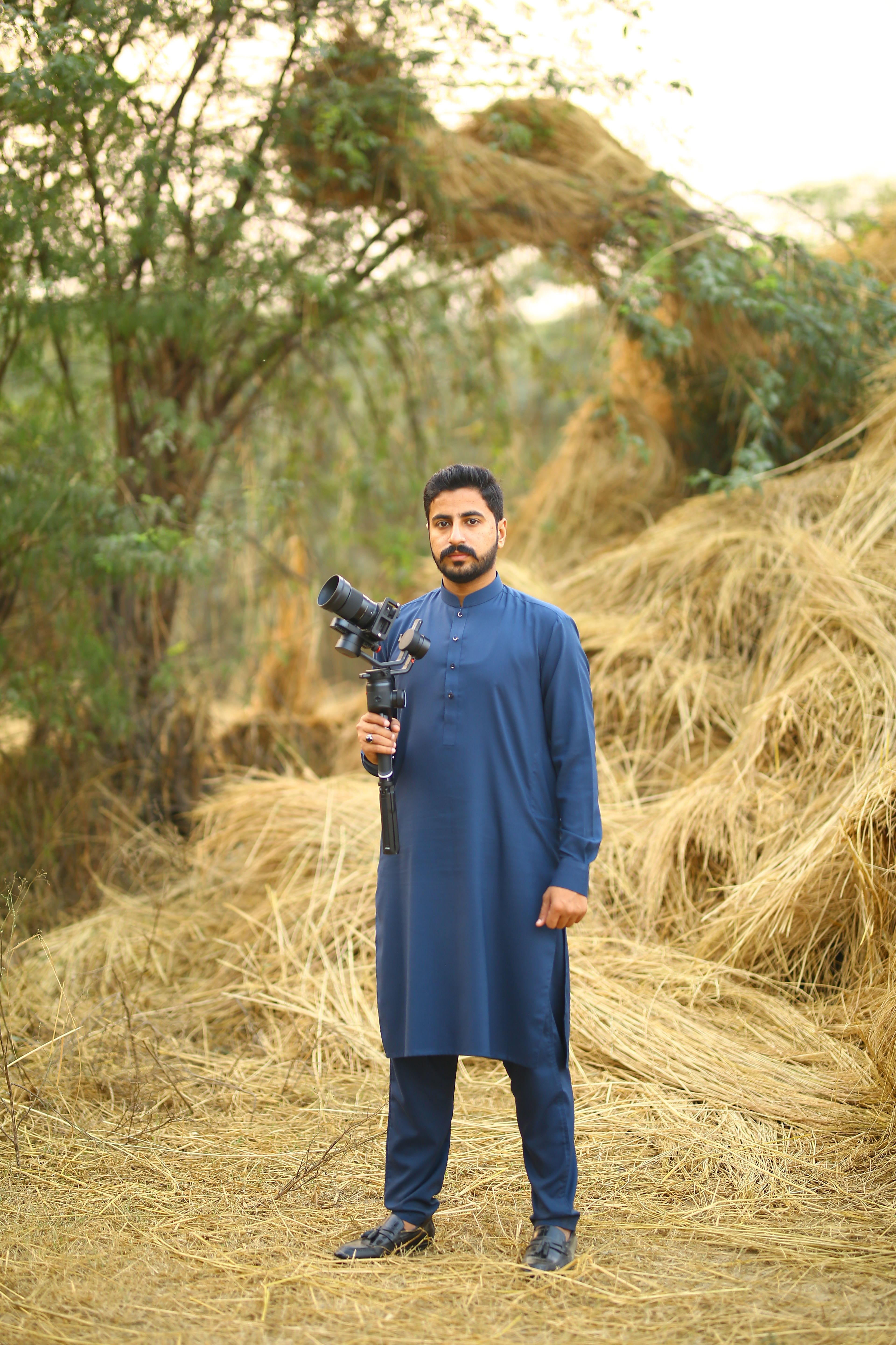 A man in traditional wear holds a camera outdoors in Kasur, Pakistan.