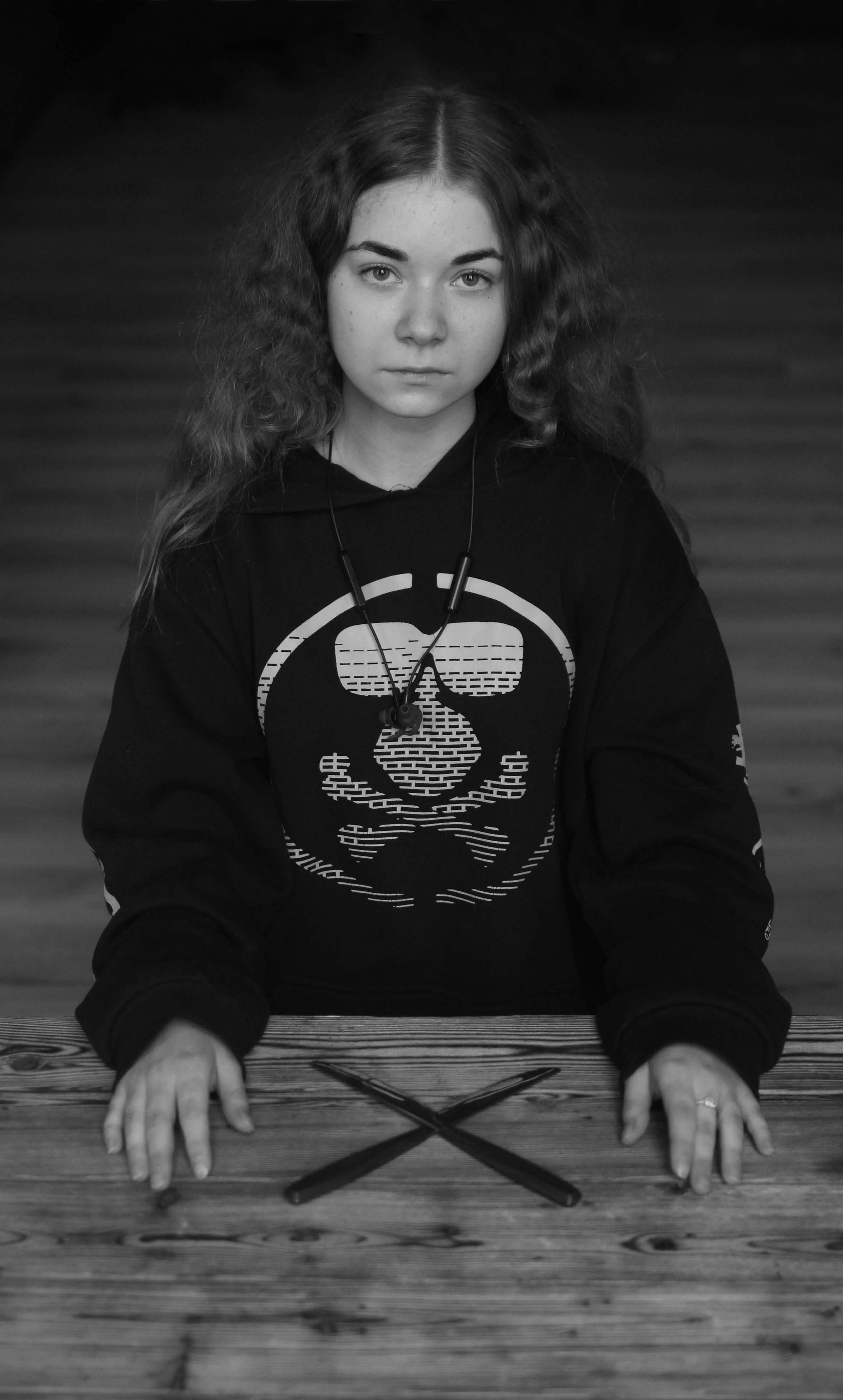 Grayscale portrait of a young woman in a black sweatshirt, seated at a wooden table.