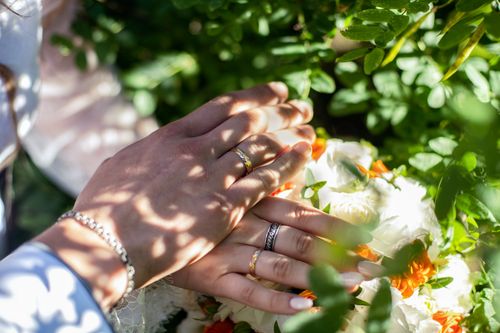 Free Close-up of hands with wedding rings resting on a vibrant floral bouquet outdoors. Stock Photo
