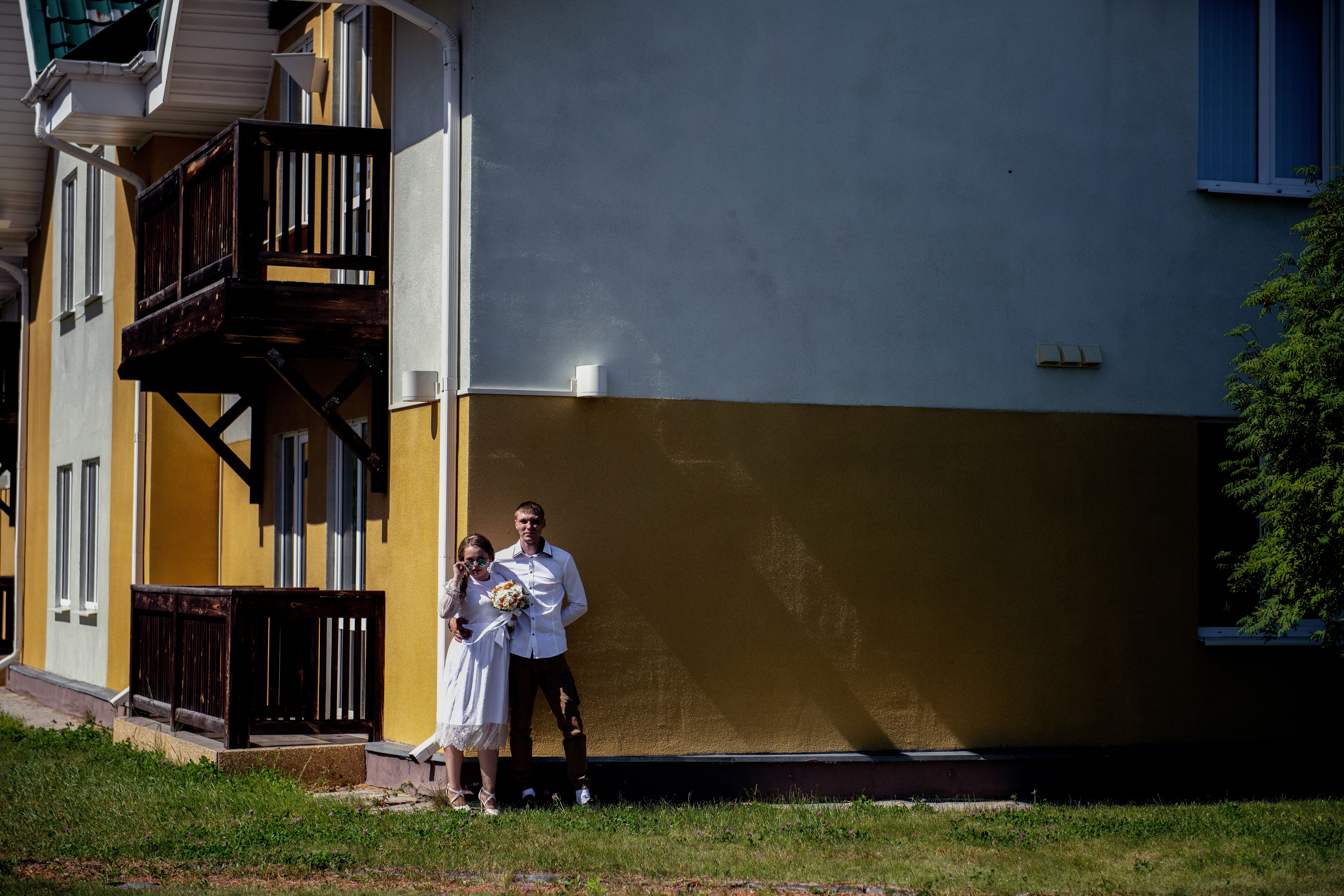 A bride and groom share a moment outside a house, captured in bright daylight.
