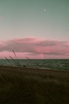 Romantic twilight beach scene with pink clouds, calm sea, and moon overhead.