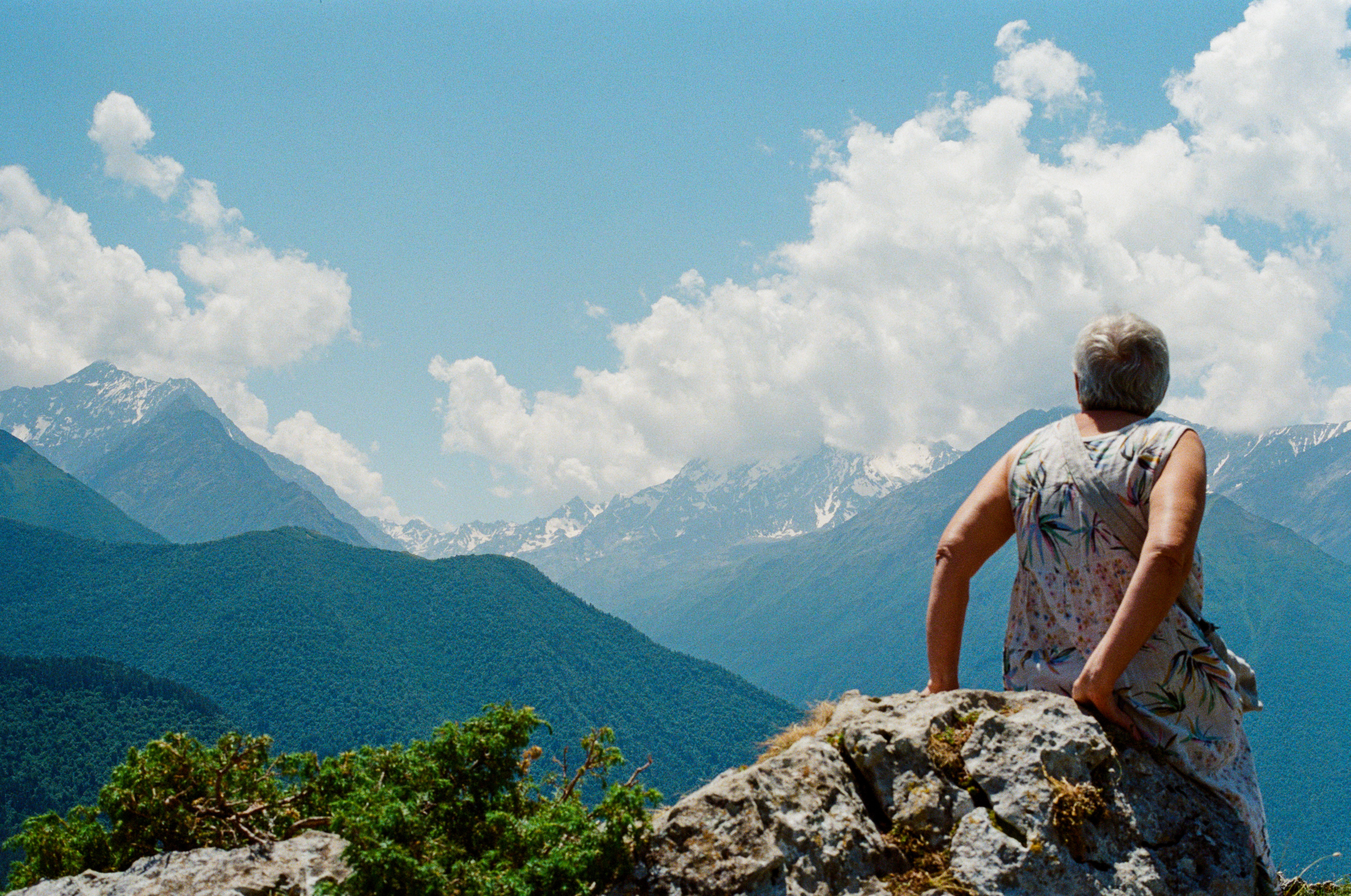Elderly woman enjoying the view from the top of a mountain under a bright blue sky.