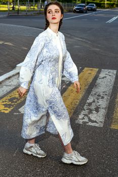 Woman in a printed dress walking confidently on a city crosswalk during the day.