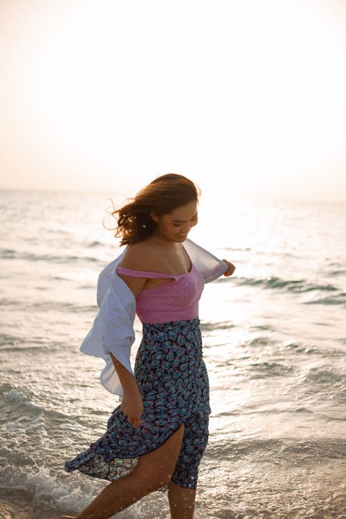 Free A woman in summer attire walks along the beach at sunset, enjoying the waves. Stock Photo