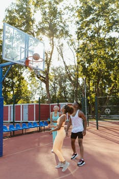 A dynamic group of young adults playing basketball on an outdoor court during a sunny day.