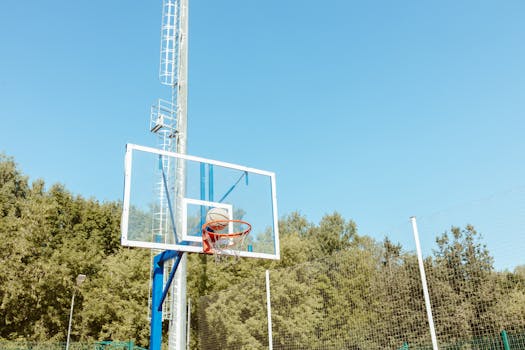 Basketball on hoop outdoors under a clear blue sky, showcasing sports and activity.