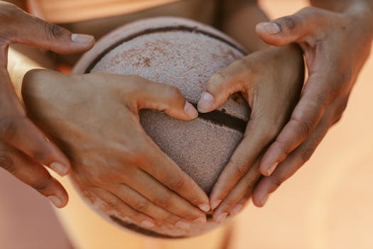 A close-up of diverse hands forming a heart shape around a basketball, symbolizing unity and teamwork.