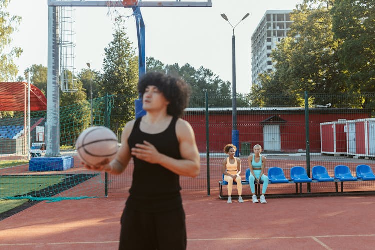 Women Sitting On Bleachers Watching A Man Holding Basketball