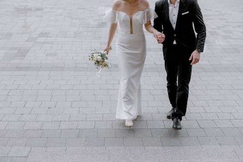 Man in Black Suit Holding Hand of Woman in White Wedding Dress