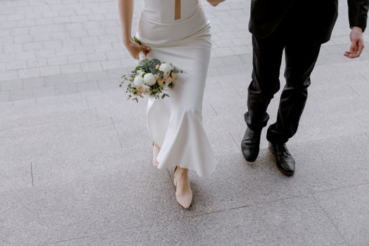 Bride and groom walking up the steps holding a bouquet and dressed elegantly.