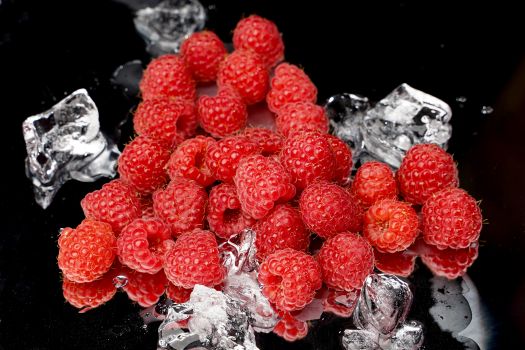Juicy raspberries and ice cubes on a glossy black surface. Perfect for food photography.