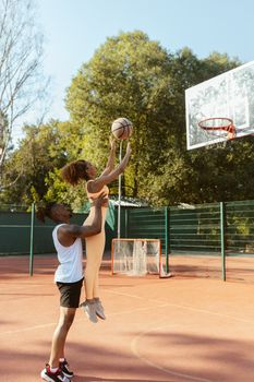Two athletes practice basketball shots outdoors on a sunny day.
