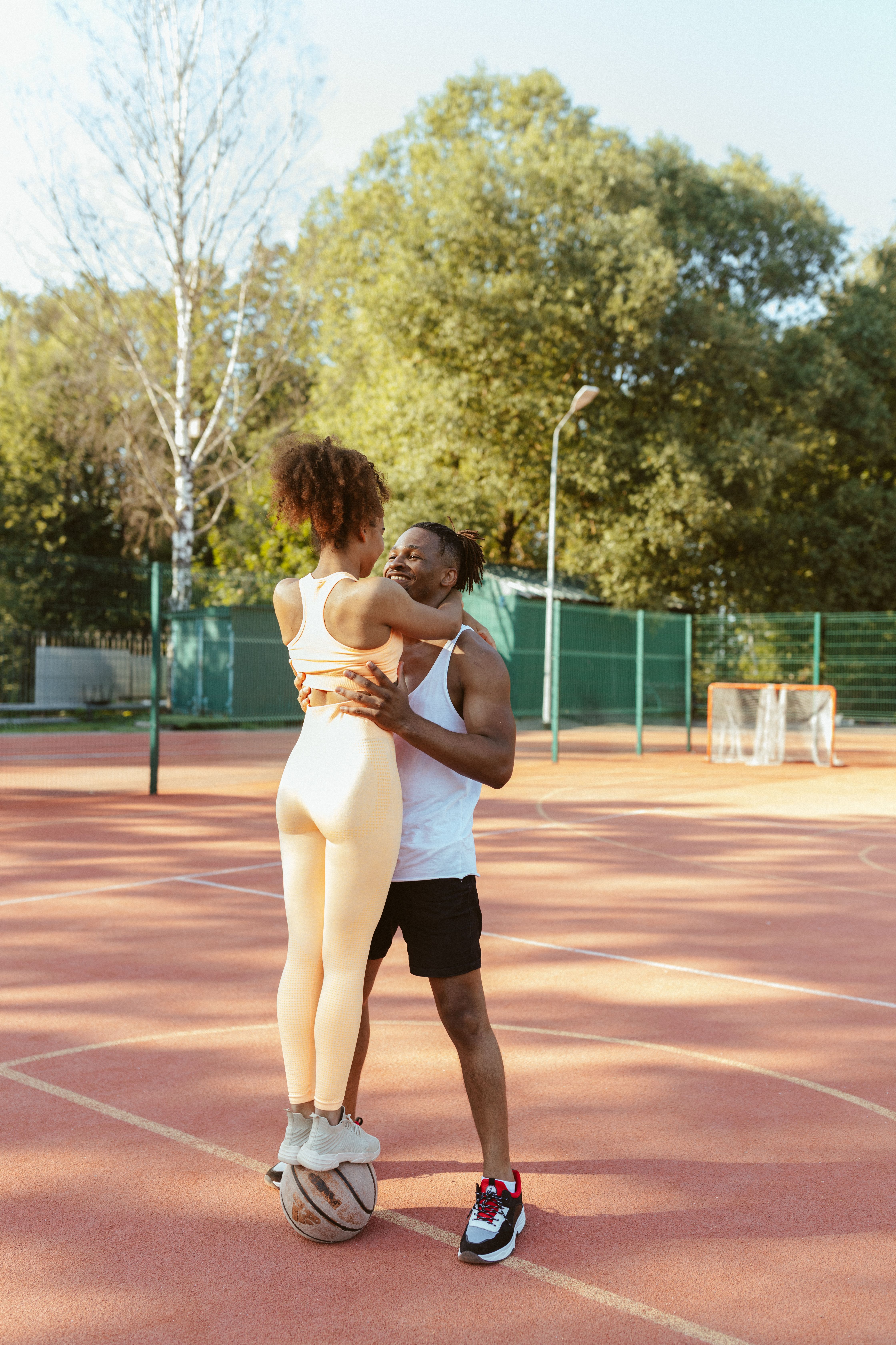 Affectionate couple sharing a moment on an outdoor basketball court in the sunlight.