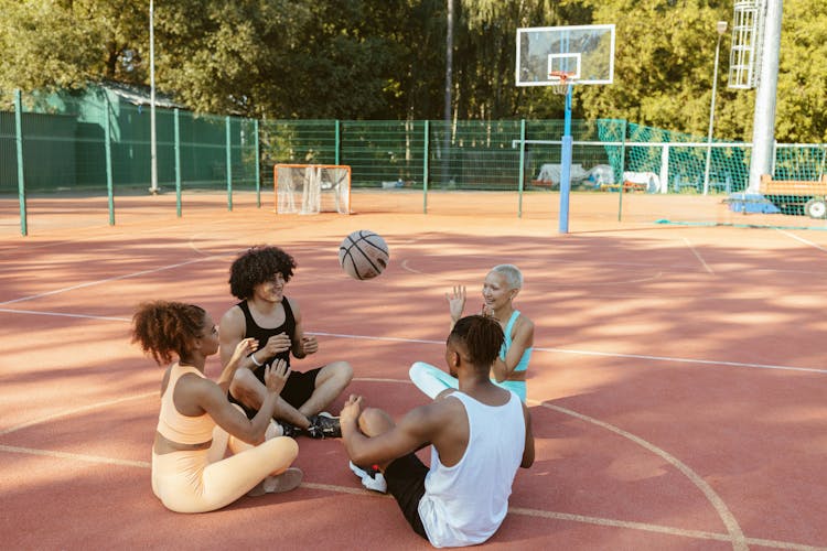 Men And Woman Sitting On Ground While Playing Basketball Ball 