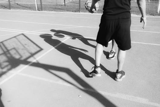 Monochrome shot of two men playing basketball, highlighting their shadows.