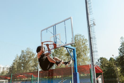 Man hanging on a basketball hoop after an impressive dunk on an outdoor court.