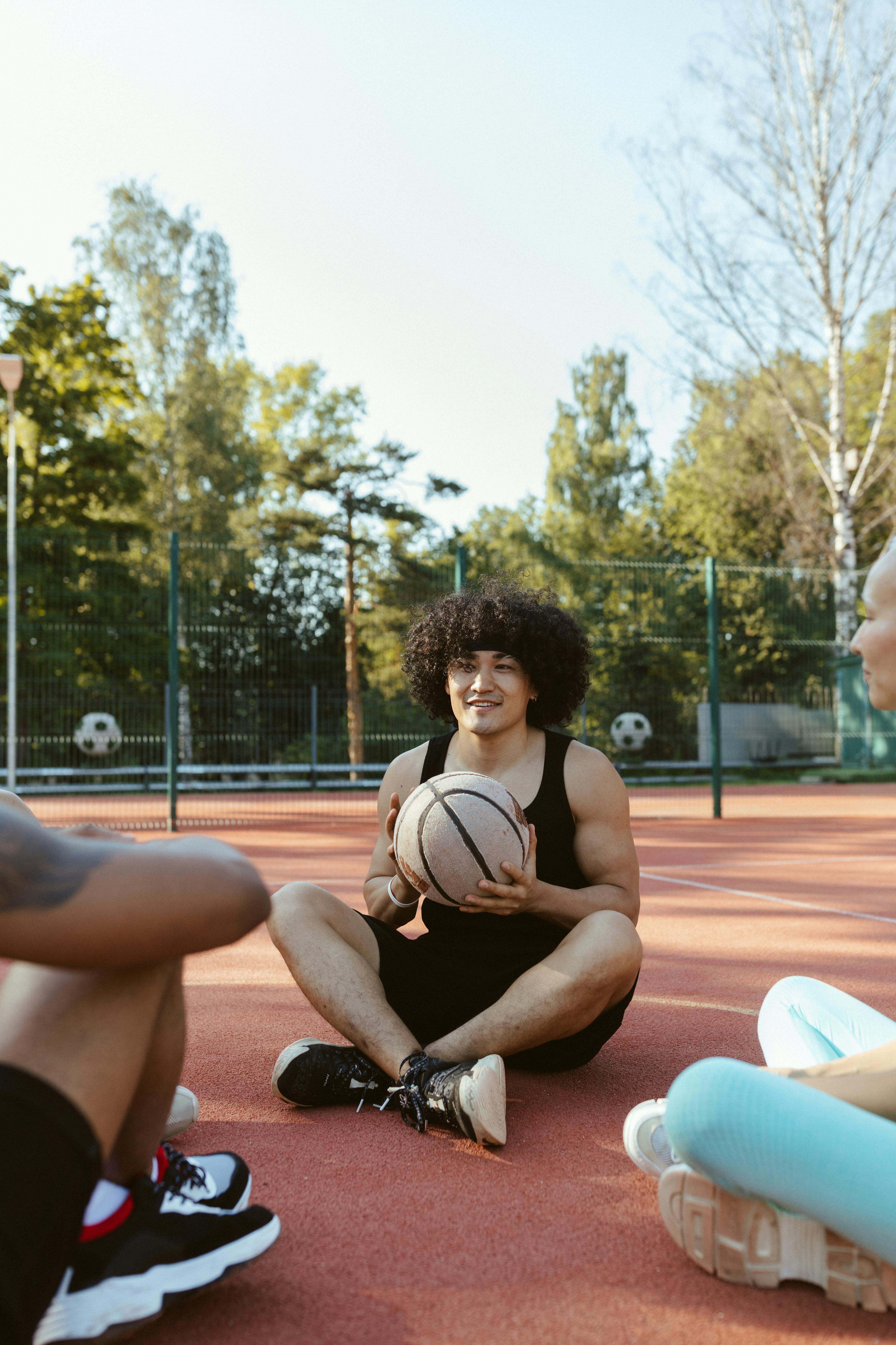an afro haired man in black tank top sitting on the basketball court